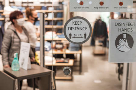 Instruction about safe shopping on the door into the shop in the gallery during Covid-19 pandemic. Behind glass door two women customers with face masks.の写真素材