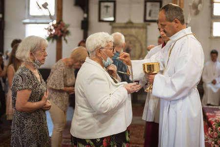 LUBIN, POLAND - JULY 19, 2020. Holy Mass in the Church. The priest gives holy communion. Due to the pandemic Covid-19 coronavirus people have face masks.のeditorial素材