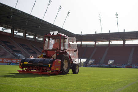 A man in a tractor with a disc seeder drill sowing grass on a football fieldのeditorial素材