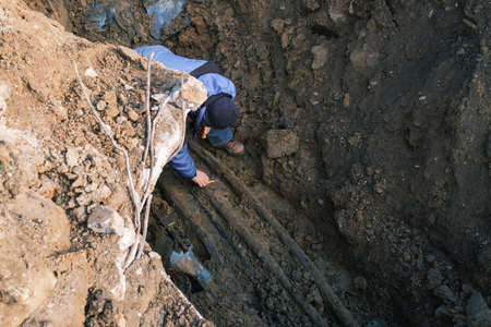 An electrician checks old electrical wiring in a trench in the ground