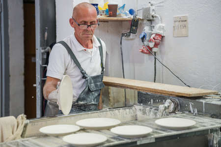 BOLESLAWIEC, POLAND - AUGUST 22, 2021: A Worker of a ceramics factory Manufaktura shows glazing of ceramics during the Pottery Festival in BolesÅawiec.のeditorial素材