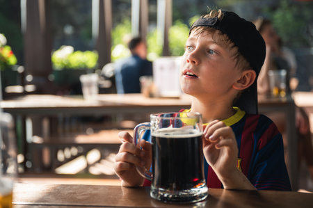 Cute boy is drinking a black drink from a large mug at a restaurant outdoor tableの写真素材
