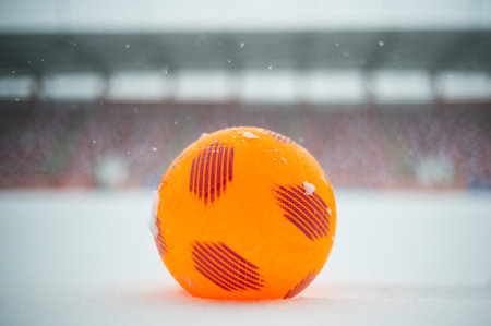 Orange soccer ball lying on the snow at football pitchの写真素材
