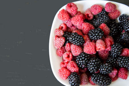 berries. Fresh berries raspberries and blackberries on a white plate on a dark background. Copy space.
の写真素材