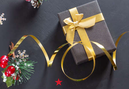 Christmas gift box with a gold bow on a black background. Spruce branch with red berries. Copyspaceの写真素材