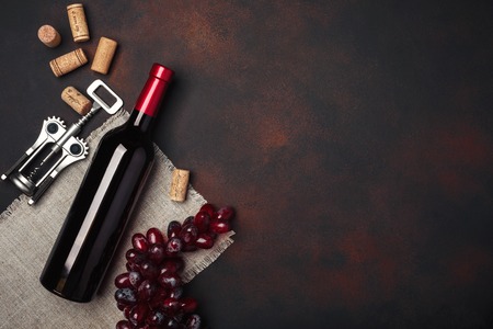 Bottle of wine, red grapes, corkscrew and corks, on rusty background top viewの写真素材
