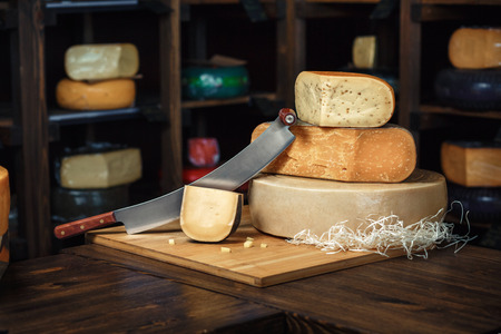 Cheese heads with slices and knives lie on a wooden board with an interiorの写真素材