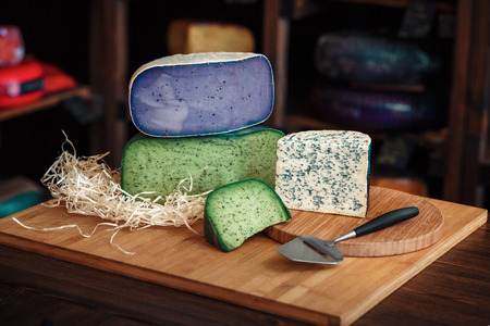 Cheese heads with slices and knives lie on a wooden board with an interiorの写真素材