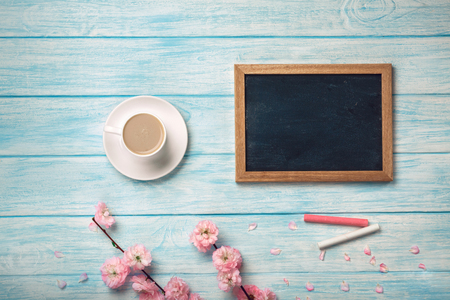 White cup with cappuccino, sakura flowers and chalk board on a blue wooden table. Top view.の写真素材
