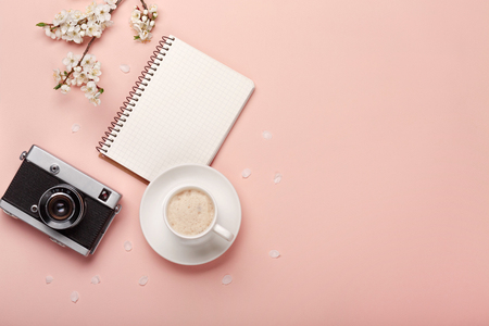 A white cappuccino cup with sakura flowers, notebook , headphones, pen on pink background. View from aboveの写真素材