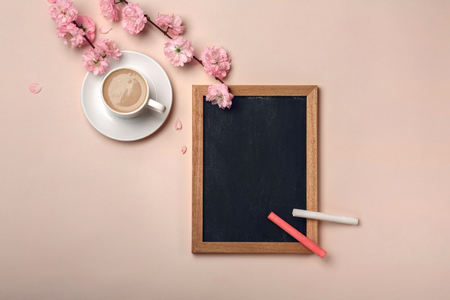 White cup with cappuccino, sakura flowers, chalk board on a pastel pink background. Top view.の写真素材