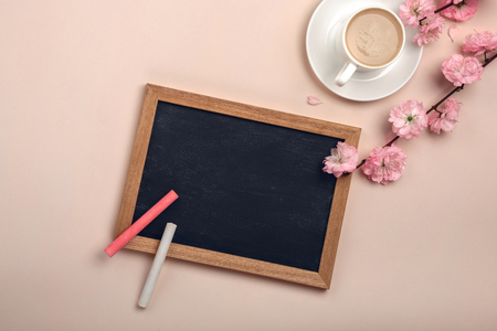 White cup with cappuccino, sakura flowers, chalk board on a pastel pink background. Top view.の写真素材