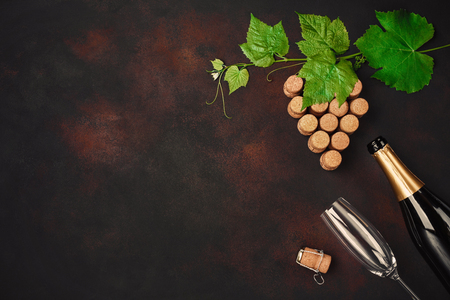 Bottle of champagne, gape bunch of cork with leaves and wineglass on rusty background top view.の写真素材