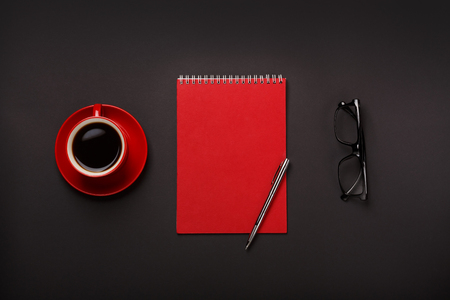 Black background red coffee cup notepad pen glasses empty place desktop. Top viewの写真素材