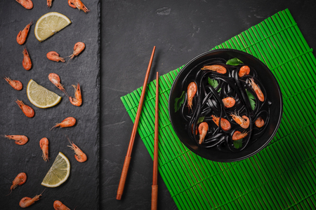 Black squid ink Fettuccine pasta with prawns or shrimps , parsley, chili in wine and butter sauce. Top view on graniteの写真素材