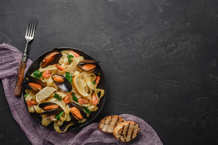 Spaghetti vongole, Italian seafood pasta with clams and mussels, in plate with herbs and glass of white wine on rustic stone background. Traditional Italian sea cuisine, close-up, top view. Copy spaceの写真素材