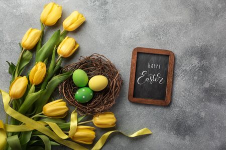 Easter background with blue and pink eggs in nest and yellow tulips. Top view with space for your greetings.のeditorial素材