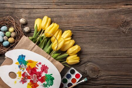 Yellow tulips, a nest with Easter eggs, bright colors and a palette on a wooden background. Top view with copy spaceのeditorial素材