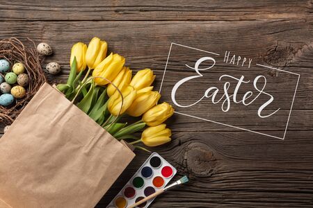 Yellow tulips, a nest with Easter eggs, bright colors and a palette on a wooden background. Top view with copy spaceのeditorial素材