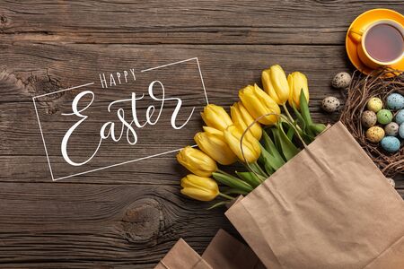Yellow tulips, a cup of tea and Easter eggs on a wooden background. Top view with copy spaceのeditorial素材