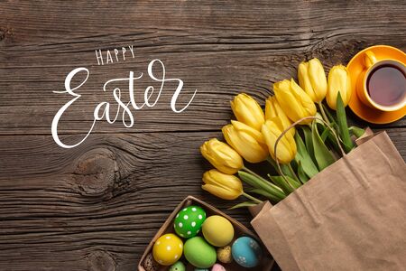 Yellow tulips in a paper bag, a nest with Easter eggs on a wooden background. Top view with copy spaceのeditorial素材