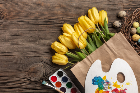 Yellow tulips, a nest with Easter eggs, bright colors and a palette on a wooden background. Top view with copy spaceの写真素材