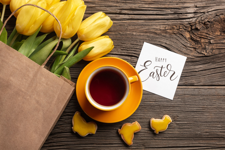 Easter gingerbread cookies, cup of tea on wooden table and yellow tulips. Greeting card. Top view with copy spaceの写真素材