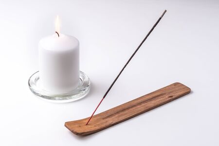 Candle and incense stick on a wooden plate with white background