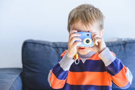 blond little boy with camera in hand and shooting photograph at home