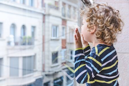 blonde little girl looks at the street from the balcony during COVID-19 confinementの写真素材