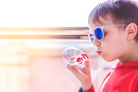 blond kid with sunglasses playing with soap bubbles near balcony