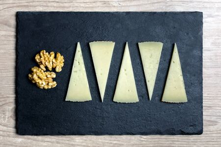 slices of spanish manchego cheese and walnuts on a dark stone plateの写真素材