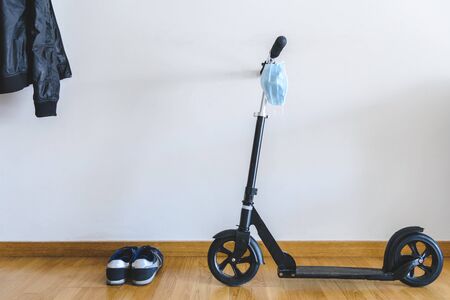 black scooter parked at home with surgical mask hanging from the handle bar. Concept of safety in...