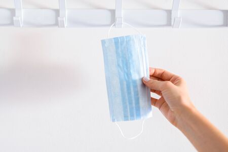 Hand of a caucasian woman taking a surgical mask from a coat rack. Concept of new normalの写真素材