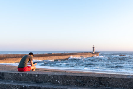 Porto, PORTUGAL - 07/10/2020: man using a tablet in beach from Foz de Douro near lighthouseのeditorial素材