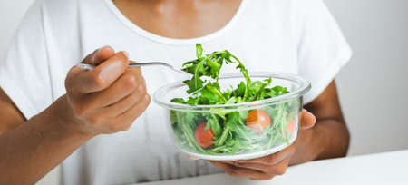 lunch box with salad hold by an unrecognizable afro female model. Laptop keyboard reflected on...