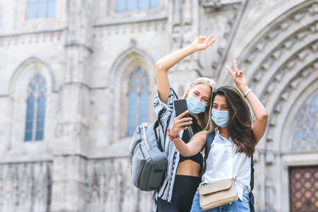 caucasian and indian female friends using smart phone to take a self portrait with Barcelona cathedral on the backgroundの写真素材
