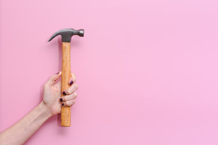 horizontal picture of the hand of a caucasian young woman holding a hammer on a pink background. Concept of equality at work and woman strength. Copy space on the rightの写真素材