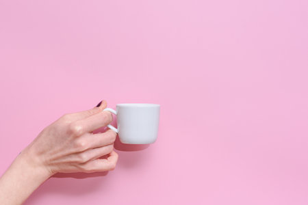 horizontal studio take of the hand of a caucasian woman holding a white cup of coffee on a pink backgroundの写真素材