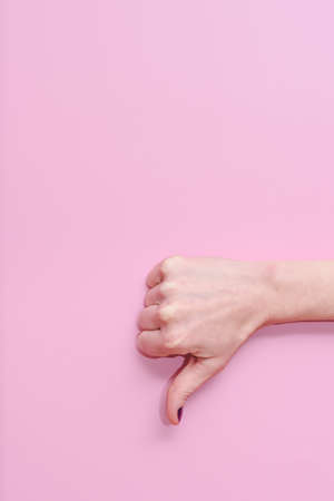 vertical take of the hand of a caucasian woman doing gesture of thumbs down on a pink background. Concept of disagreement and negativenessの写真素材