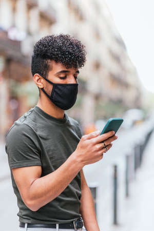 hispanic man with black mask using his phone in the streets of Barcelonaの写真素材