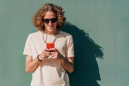 portrait of an attractive young redhead man using his smart phone near a green wallの写真素材
