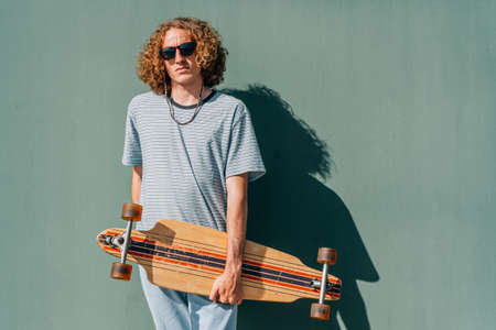 attractive young guy looking at camera with his long board on a sunny summer dayの写真素材
