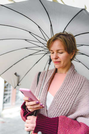 woman with umbrella using a pink smart phone on the streetの写真素材
