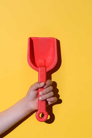 red toy shovel on the hands of a caucasian boy with yellow background