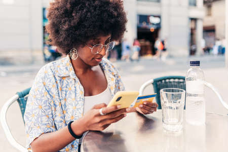 Afro american young woman paying online shopping with her credit card and phone