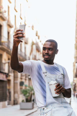 young afro man taking himself a picture in the streets of Barcelona with a smart phone