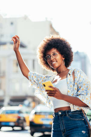 portrait of an african young woman calling a taxi on the streetsの写真素材