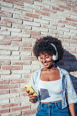 vertical portrait of an african young woman with her phone and headphones in the street
