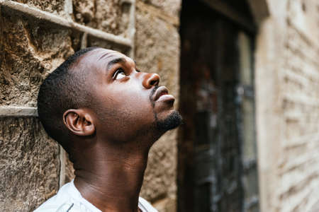 Portrait of a thoughtful young african man leaning on a wall and looking up